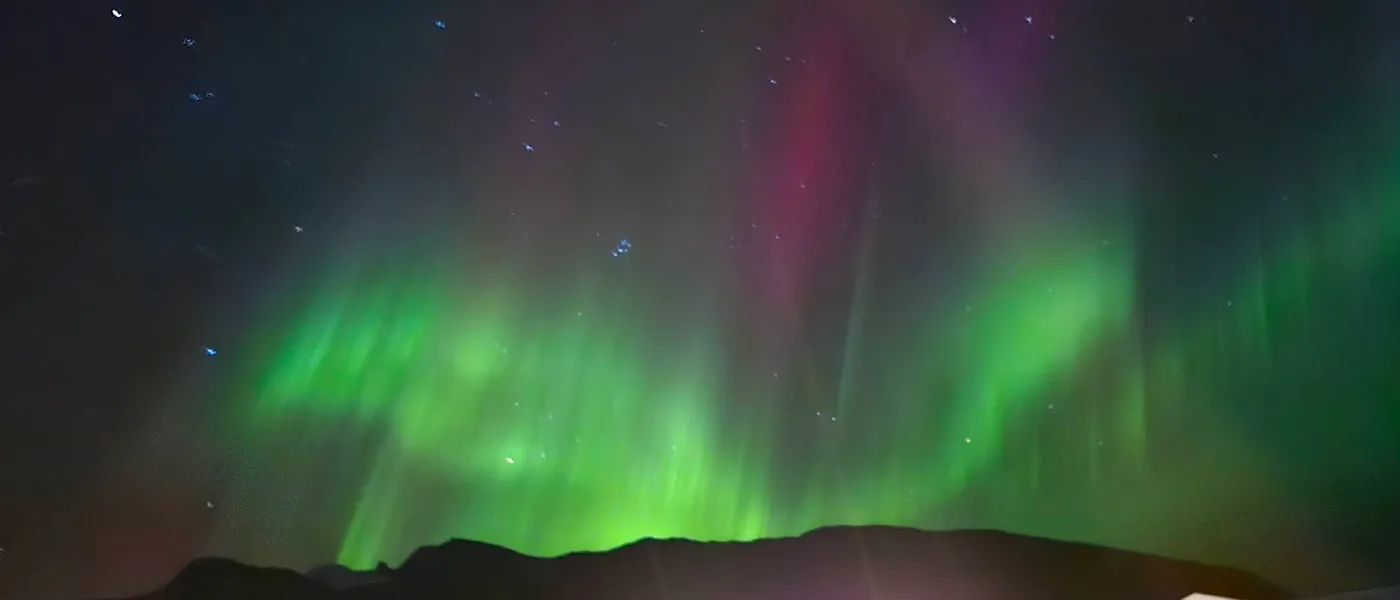 Green and pink northern lights over a dark mountain ridge under a starry sky