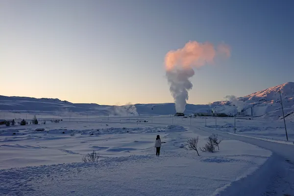 Geothermal steam rising over a snow-covered valley at dawn, a person standing in the snow watching it