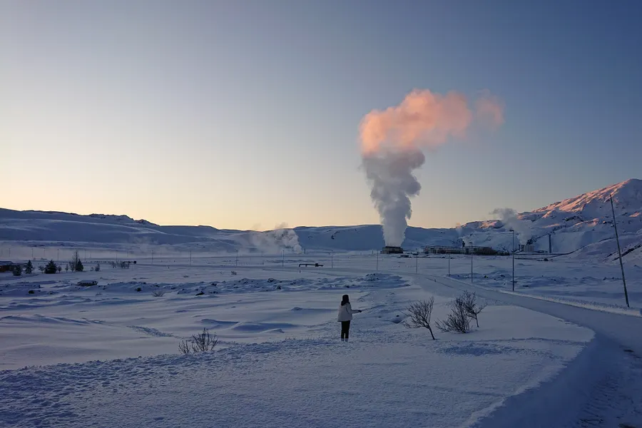 A geothermal steam plume against a snowy mountain lit by low sun
