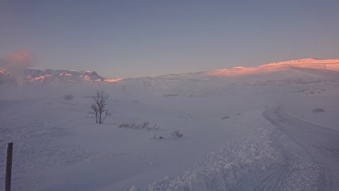 Pink dawn light on a snow-covered ridge above a snowy plain