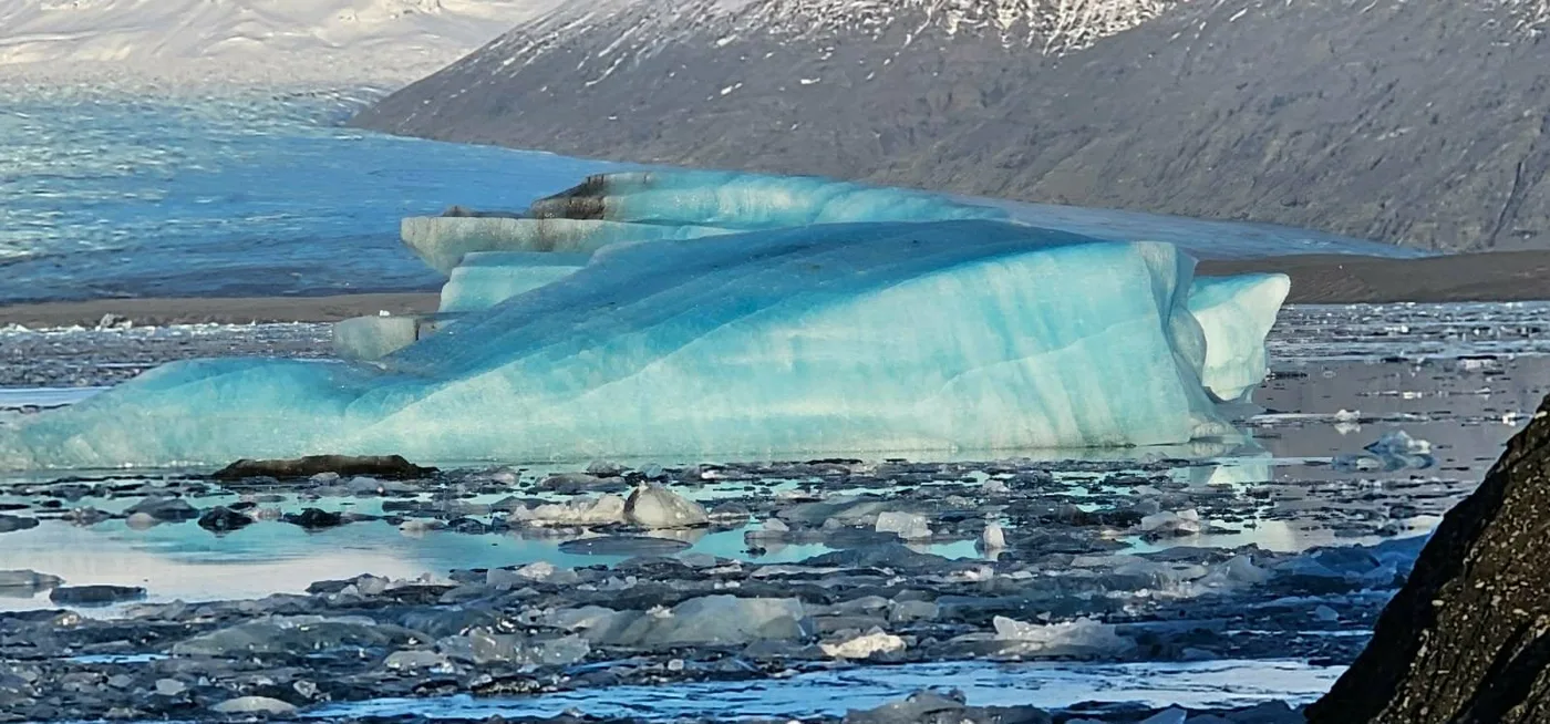A large striped blue iceberg close to the black shore of the lagoon