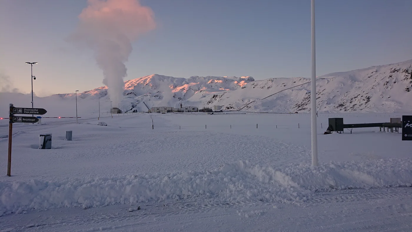 A tall white steam plume rising from the Nesjavellir geothermal plant at dawn, pink mountains behind