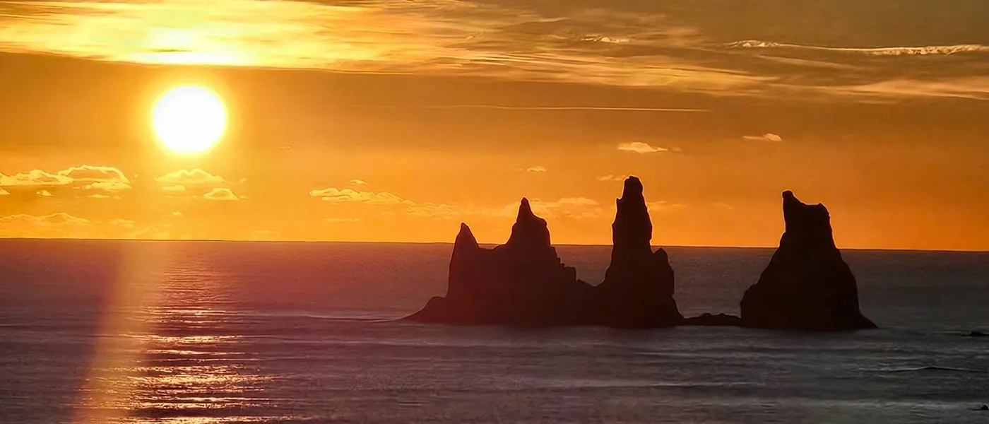 The Reynisdrangar sea stacks off Vík, black against a low orange sunset over the sea