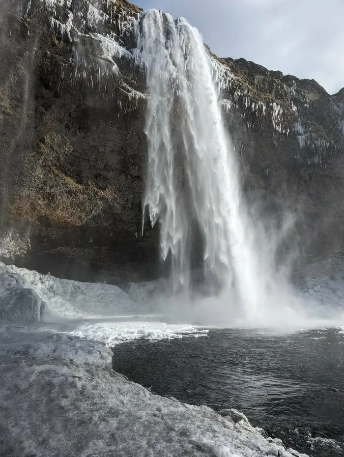 Seljalandsfoss in winter, with thick ice and snow built up around the plunge pool
