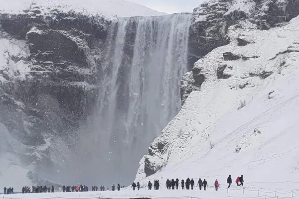 Skógafoss in winter, with people standing at the foot of the falls