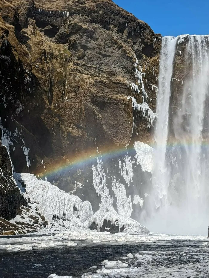 Skógafoss waterfall in winter with a rainbow across the spray and ice at its foot
