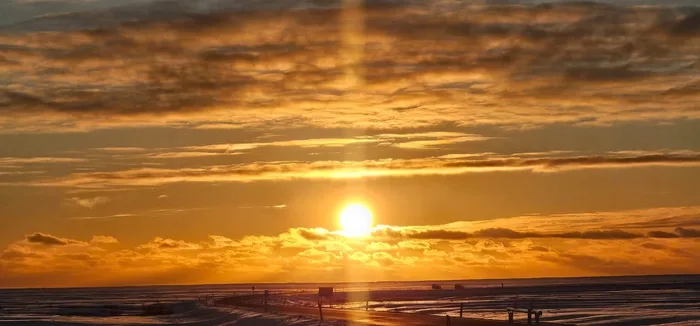 Low sun over a wide black-sand beach, the sky orange under a band of cloud