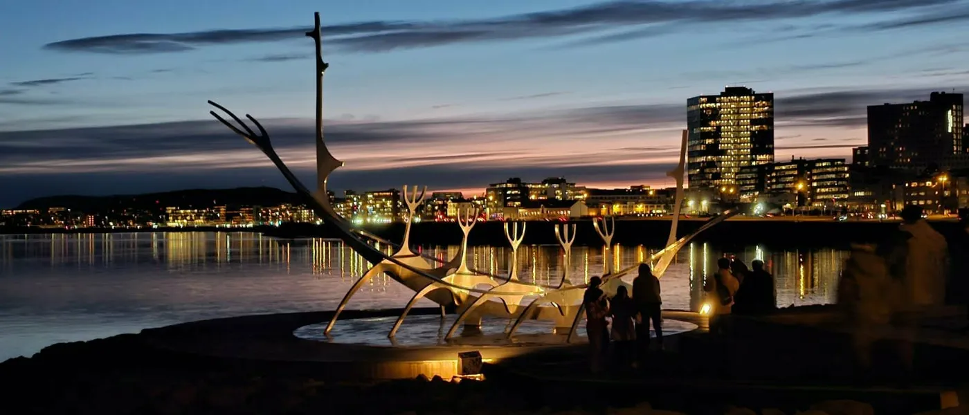 The Sun Voyager sculpture on the Reykjavík waterfront at dusk, with the city lights behind it