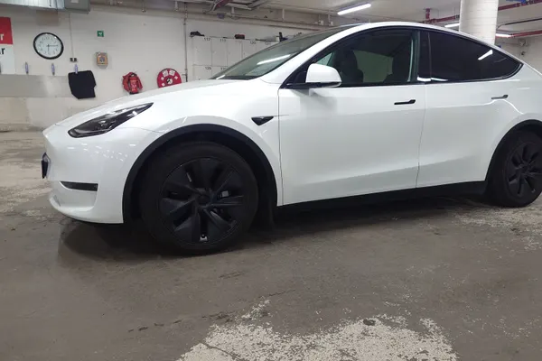 A white Tesla Model Y with a taxi sign on the roof
