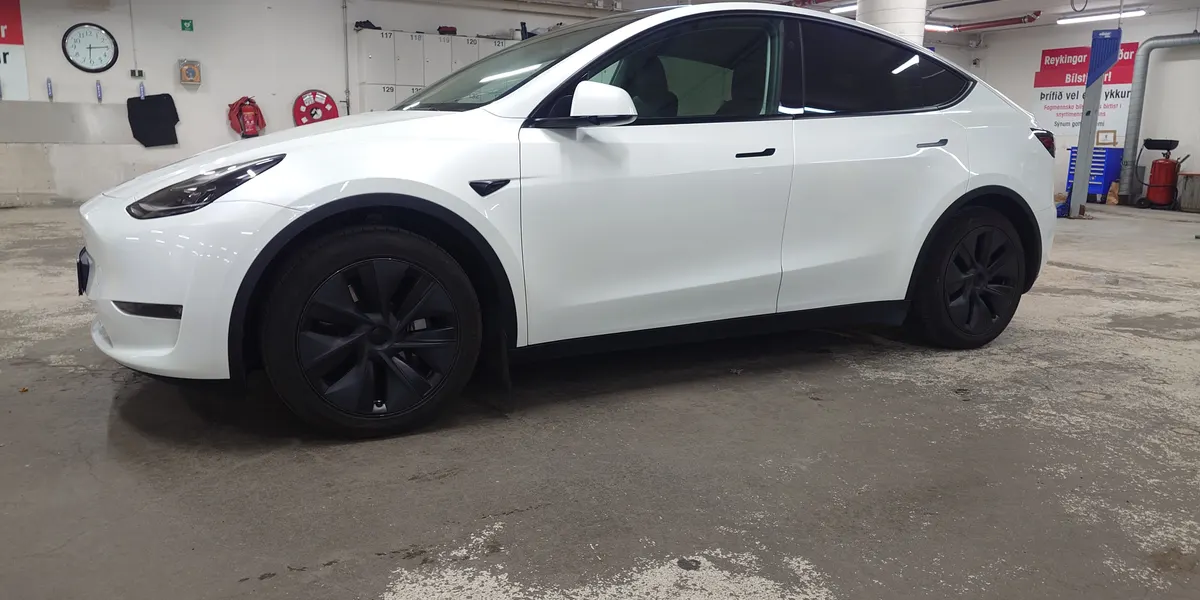 A white Tesla Model Y with a taxi sign on the roof