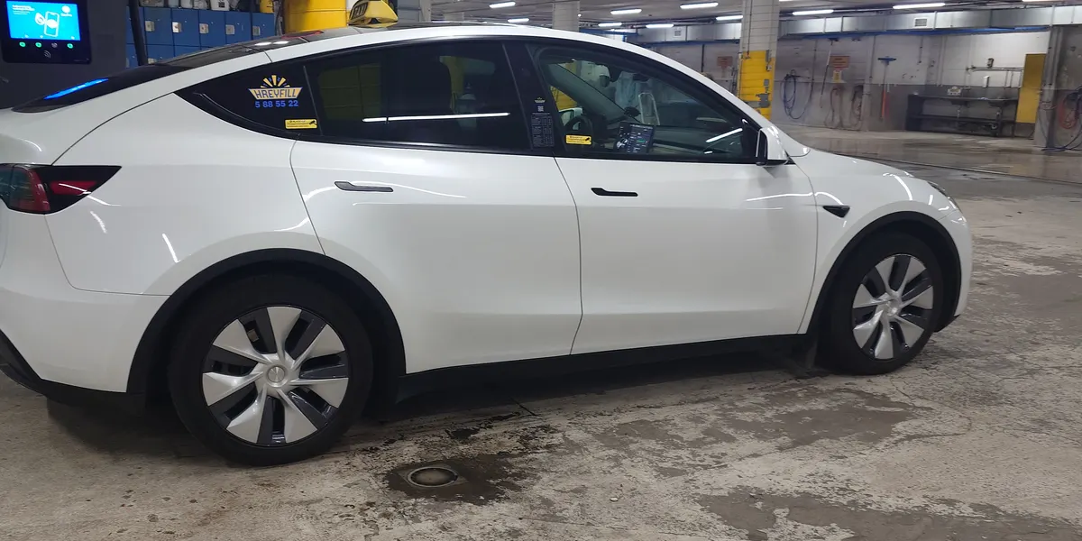 A white Tesla Model Y, licensed taxi, with the taxi sign on the roof