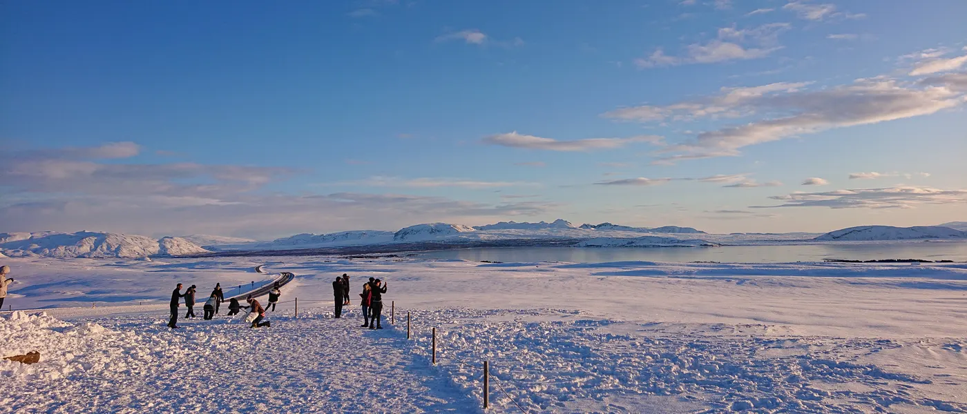 Low winter sun over Þingvallavatn, seen from a viewpoint with a handful of people at the railing