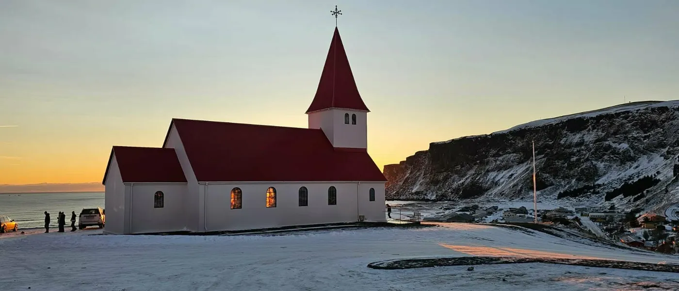 The red-roofed church at Vík í Mýrdal in snow at dusk, with the cliffs behind
